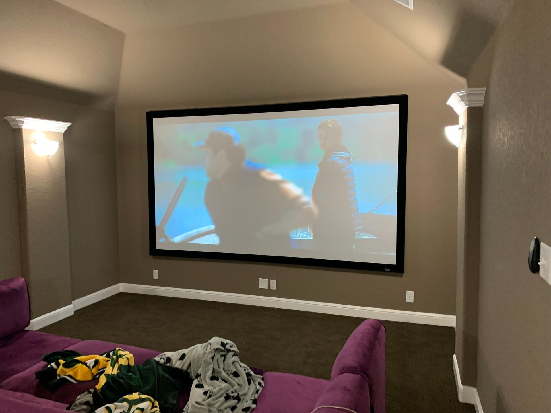A home theater with a projector screen and a purple couch.