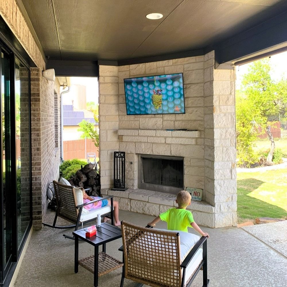 A young boy is sitting on a patio with a fireplace and a television.