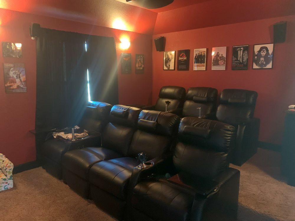 A home theater with a couch , chairs , and pictures on the wall.
