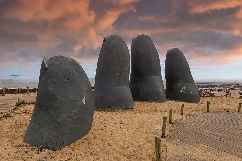 Large dark stone sculptures standing on a sandy beach under a cloudy orange sky