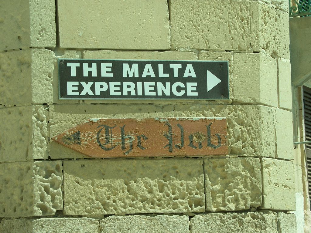 Signs on a stone wall: “THE MALTA EXPERIENCE” and “The Pub” with an arrow.