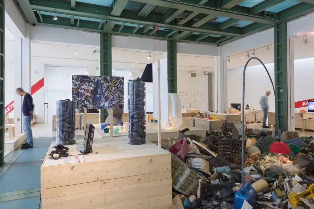 Industrial gallery with a large mound of assorted trash and debris under teal ceiling beams
