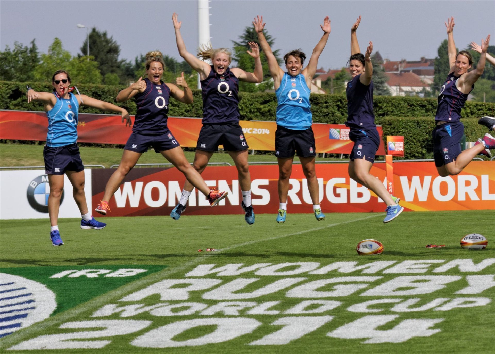 Rugby players in blue and black uniforms jump with arms raised on a field marked “Women’s Rugby World.”