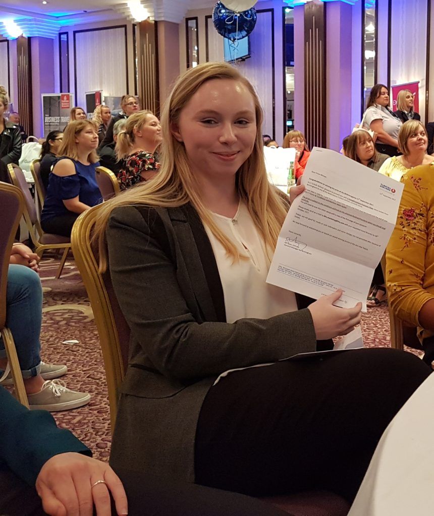 Woman seated at a banquet holding a printed program in a decorated conference room
