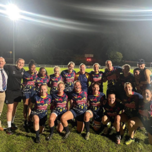 Sports team posing for a group photo on a wet field at night, wearing matching black and pink uniforms.