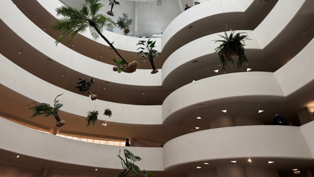 Interior of a modern multi-story atrium with curved balconies and hanging potted plants
