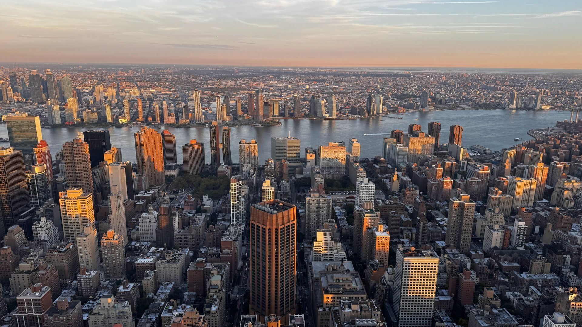 Sunlit city skyline with dense skyscrapers beside a wide river at dusk