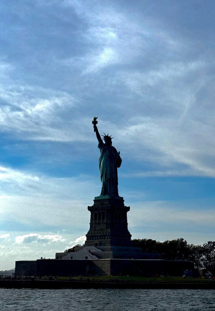 Statue of Liberty silhouetted against a cloudy blue sky at dusk