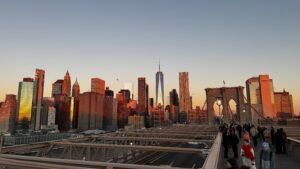 Sunset skyline with skyscrapers and Brooklyn Bridge walkway crowded with pedestrians