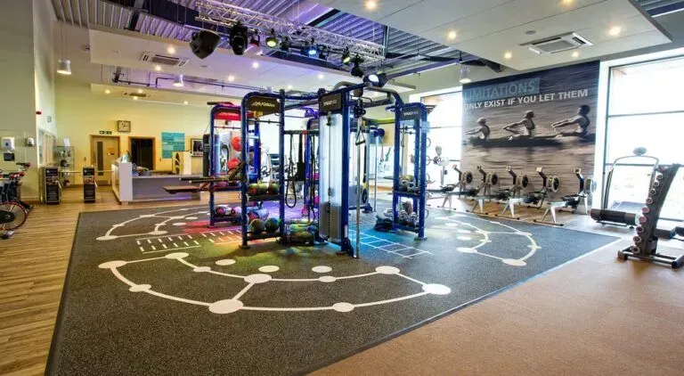 Modern gym with cable machines, treadmills, and a marked training floor under bright overhead lights