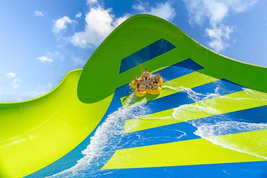 People sliding down a bright green and blue water slide under a sunny sky