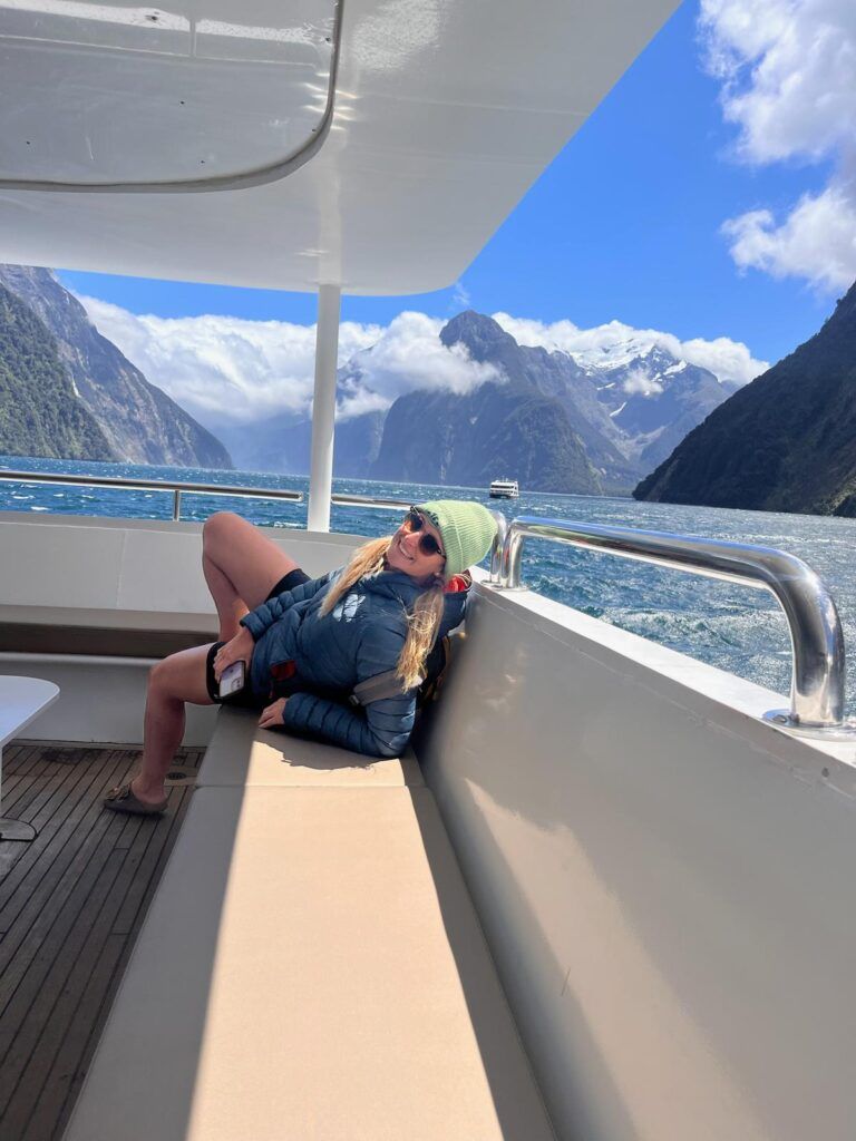 Person reclining on a boat deck with mountains and blue sky in the background