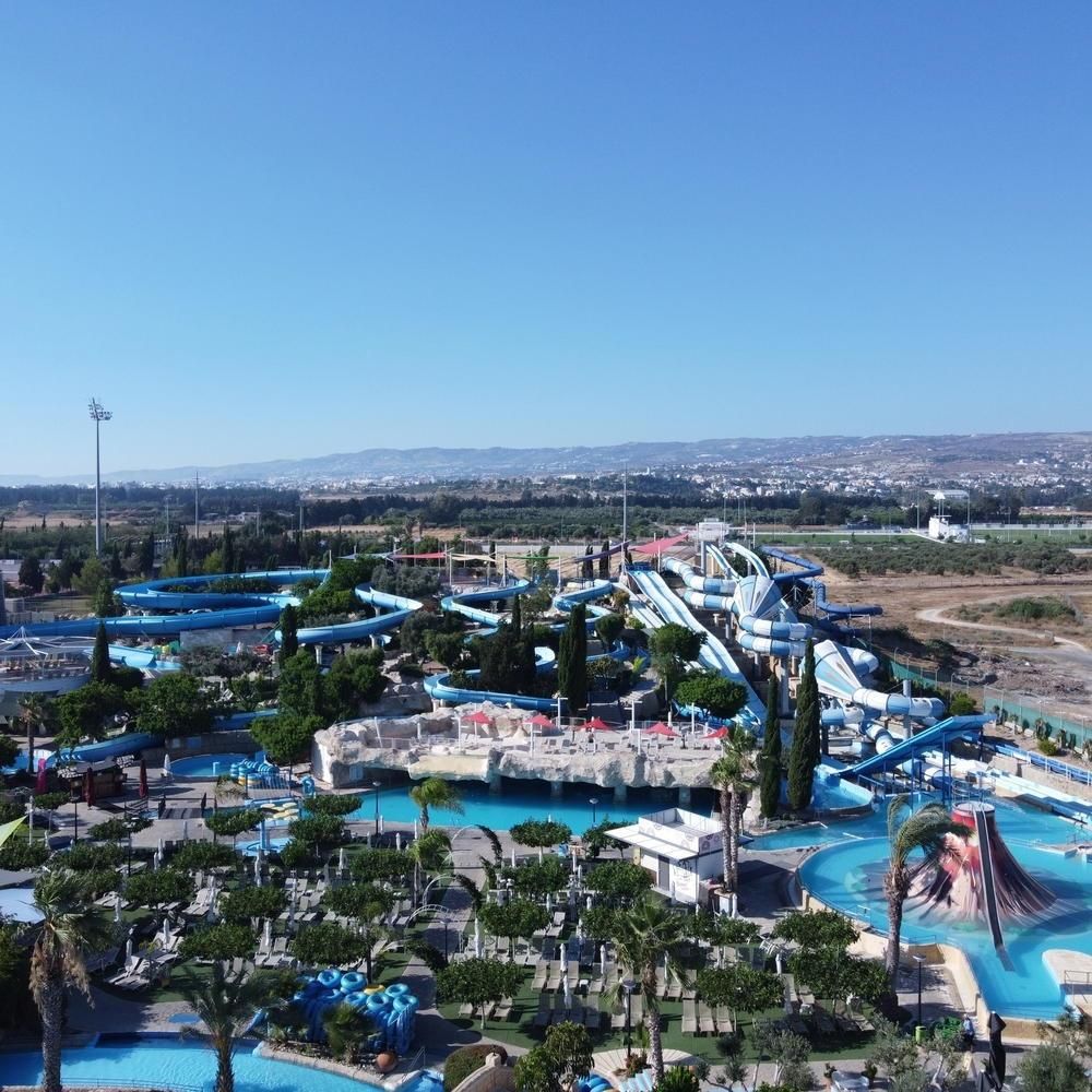 Water park with blue slides, pools, and palm trees under a clear sky, seen from above