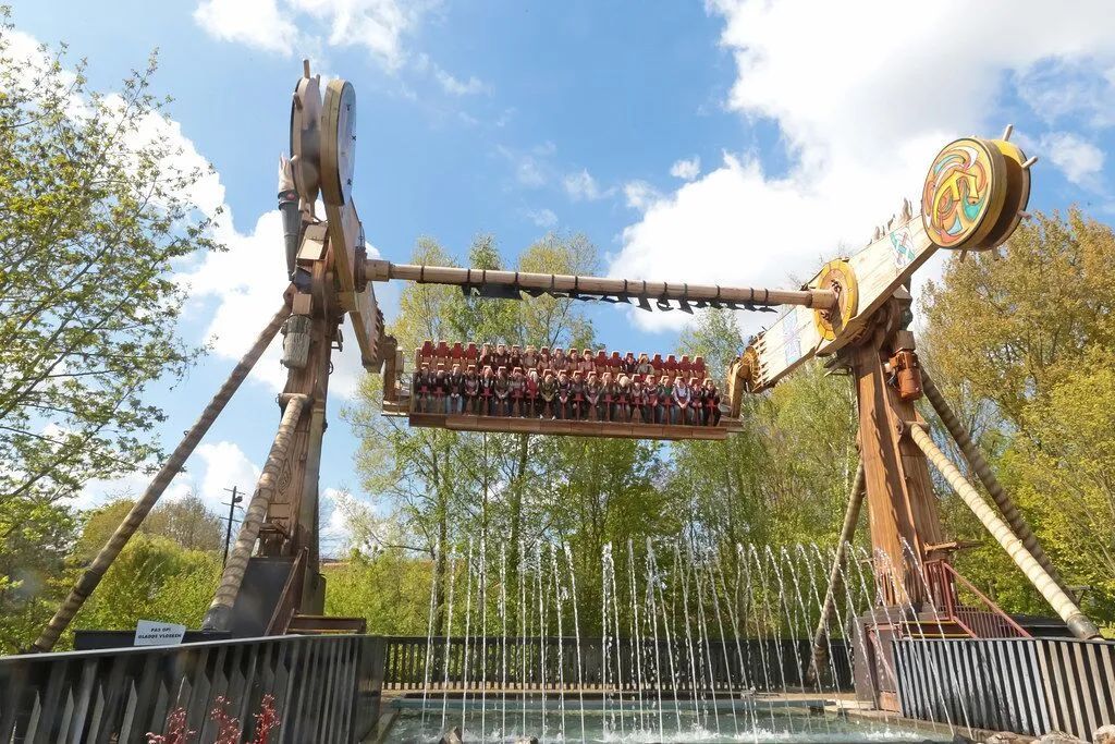 Amusement park ride with suspended seats swinging against a blue sky and trees