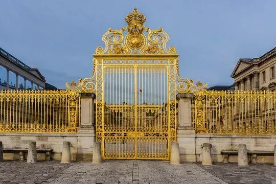 Ornate gold gate and fence before a grand palace entrance under a blue sky.