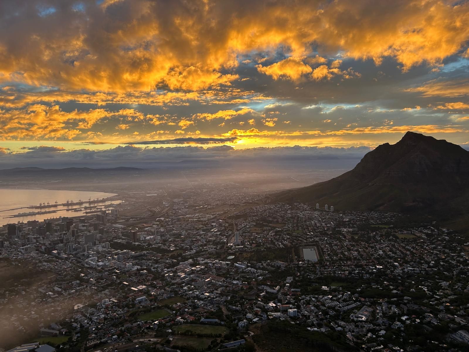 Sunset over a coastal city with a mountain silhouette and glowing orange clouds