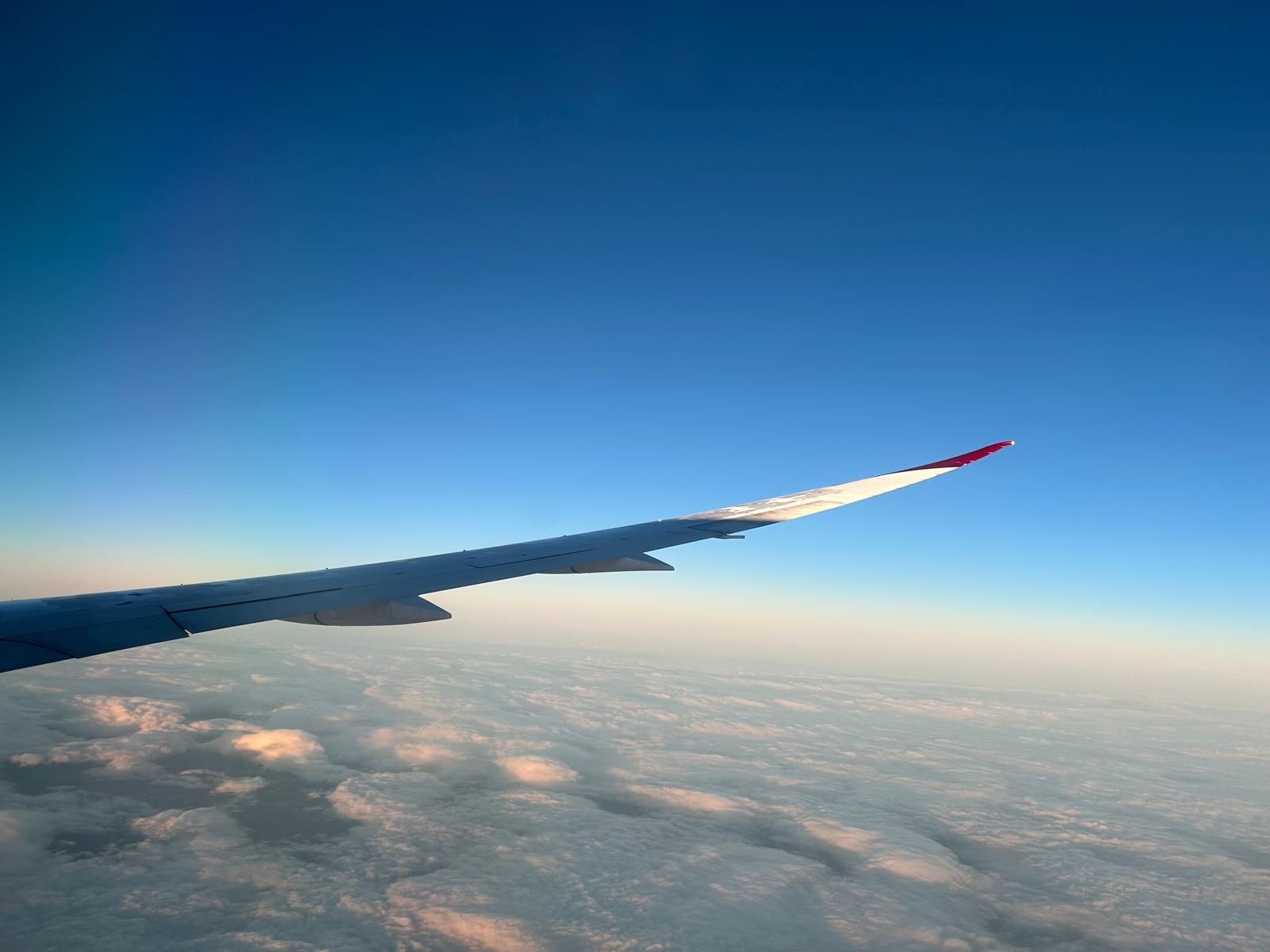 Airplane wing over clouds at sunrise with a clear blue sky