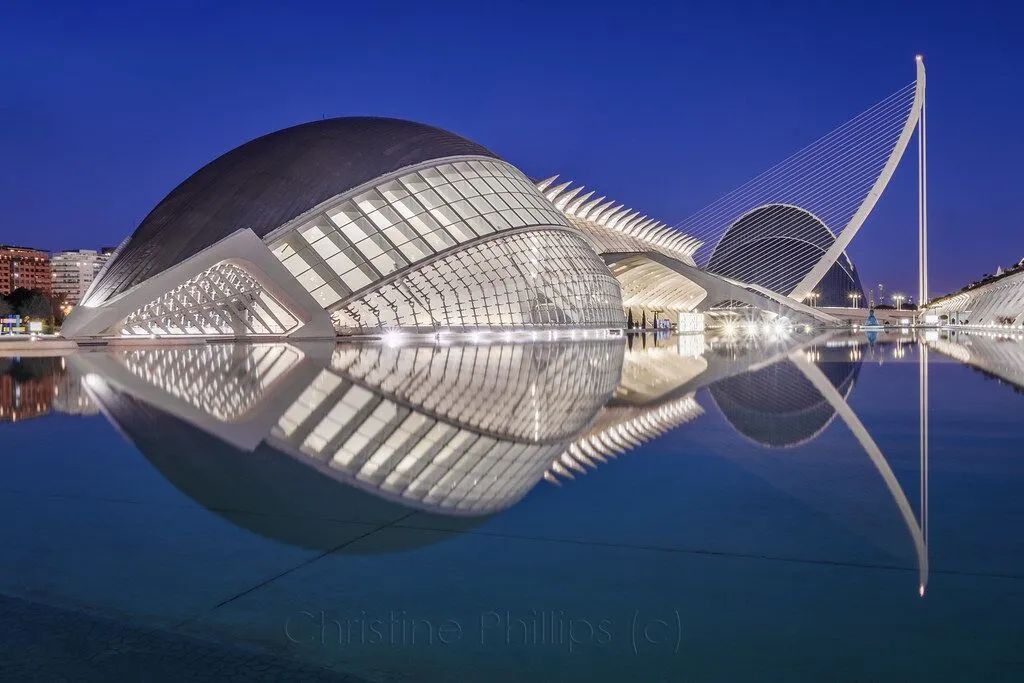 Modern architectural building with curved domes reflected in calm water at dusk