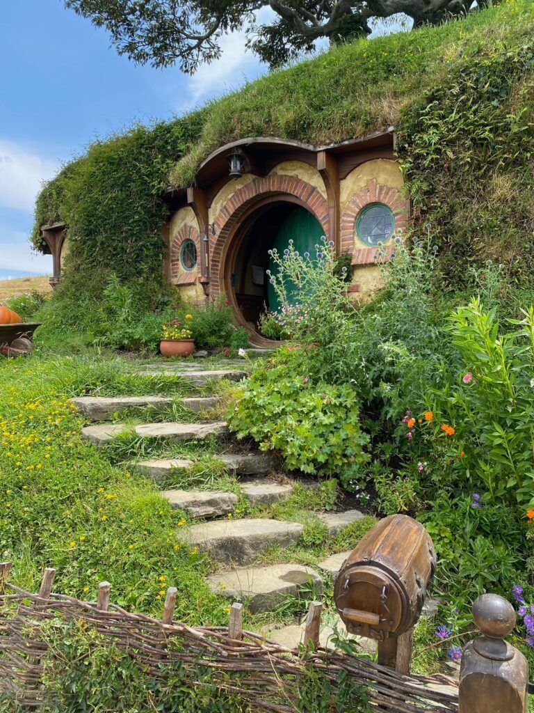 Round hobbit house with ivy-covered roof, stone steps, and lush garden path under a blue sky