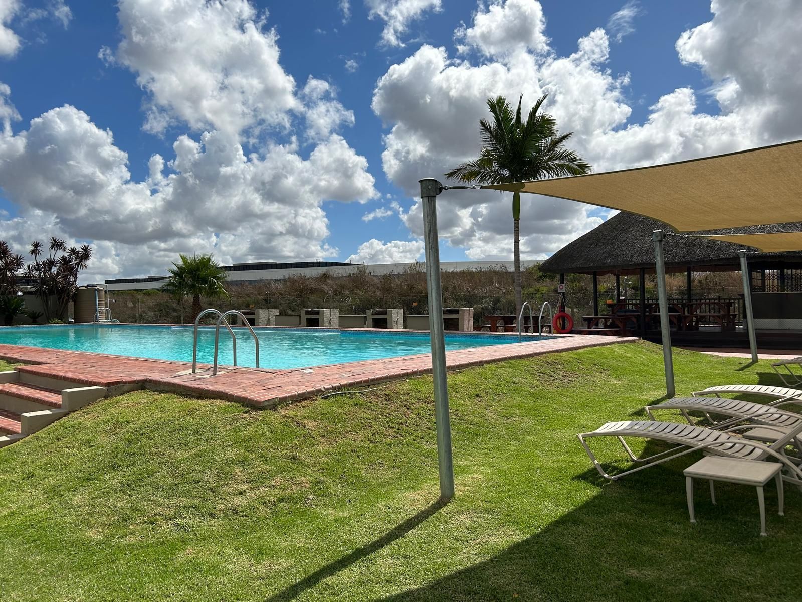 Resort pool with palm trees, lounge chairs, shaded cabana, and cloudy sky