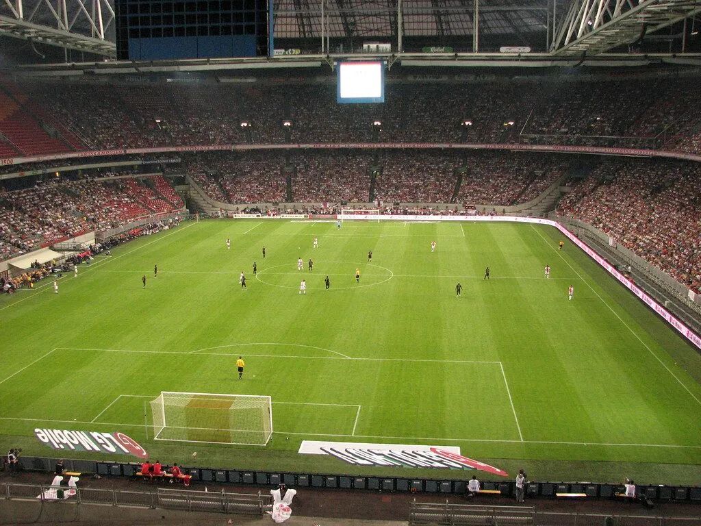 Soccer match in a packed stadium, seen from behind one goal at night.