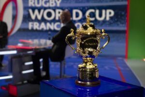 Rugby World Cup trophy on a blue podium with event signage in the background