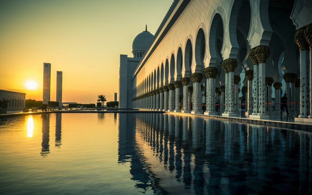 Sunset over a mosque courtyard with reflecting pool and arched colonnade