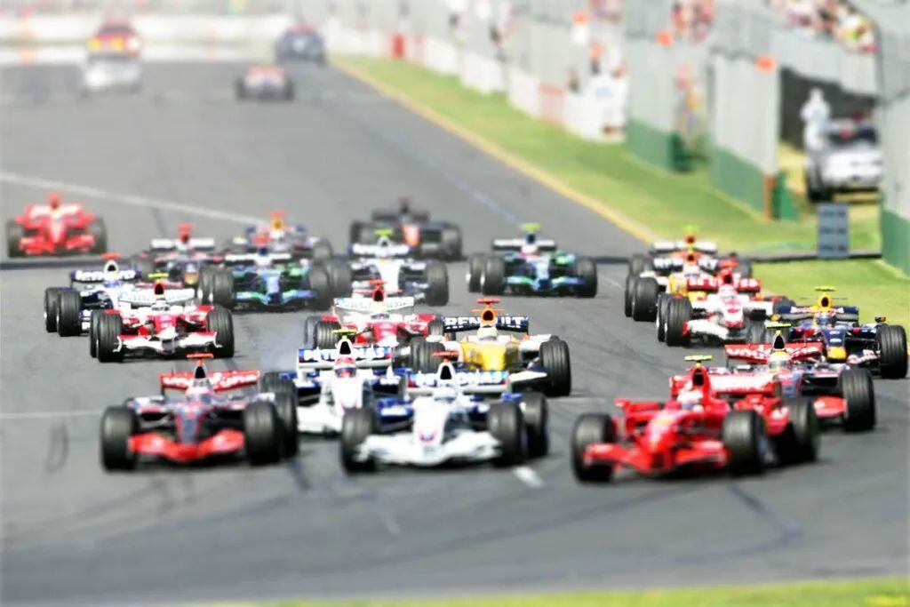 Formula 1 race cars speeding around a track, with a pack of red, white, and black cars closely grouped.
