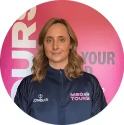 Person in a navy MSG Tours jacket standing before a pink event backdrop with logo text.