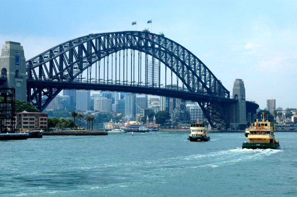 Sydney Harbour Bridge over blue water with ferries in the harbor and city skyline in the background
