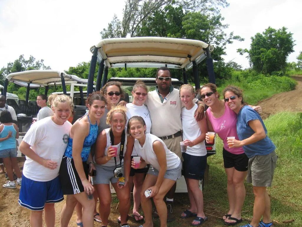 Group of smiling people posing together outdoors on a dirt road beside safari vehicles.