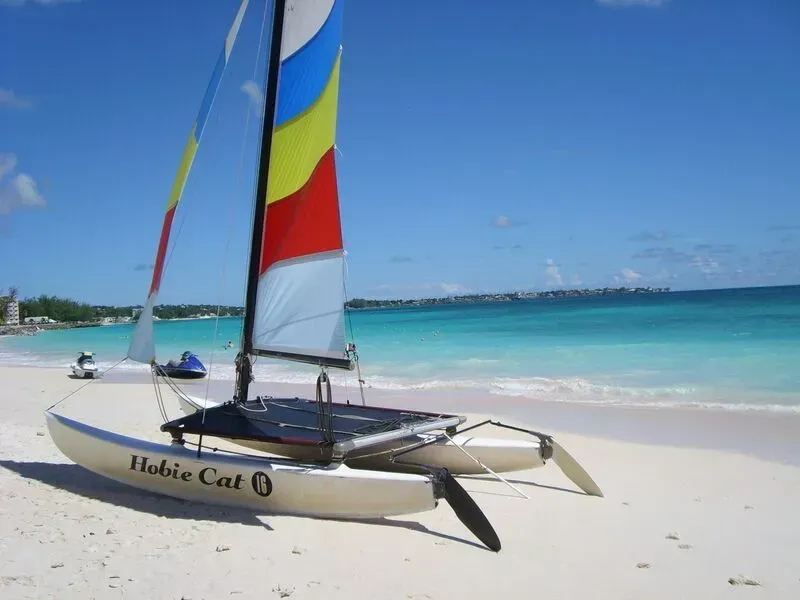 Catamaran with colorful sails on a sunny tropical beach with turquoise water.