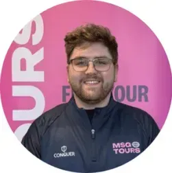 Smiling person in glasses and navy MSG Tours jacket in front of a pink branded backdrop