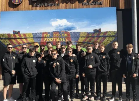 Group of people in black outfits posing outside a football stadium under a bright sky