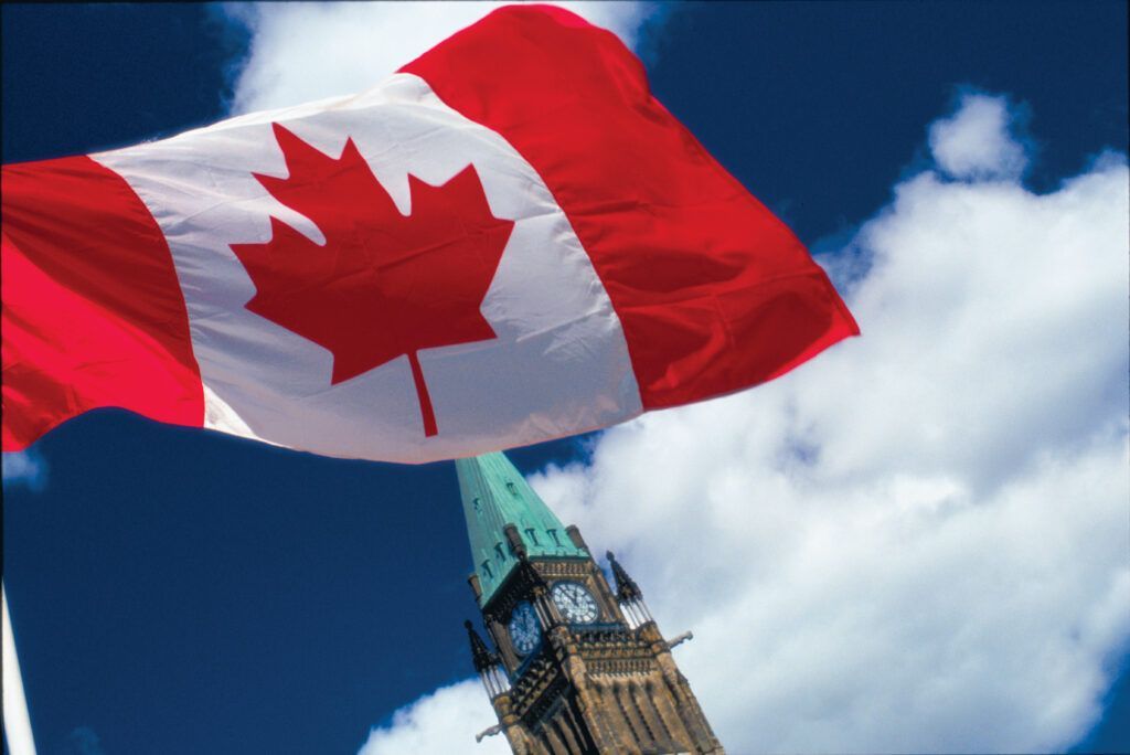 Canadian flag waving above Ottawa's Parliament building against a blue sky