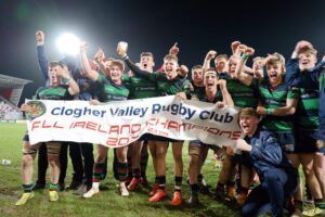Clogher Valley Rugby Club players celebrate holding a championship banner and trophy at night