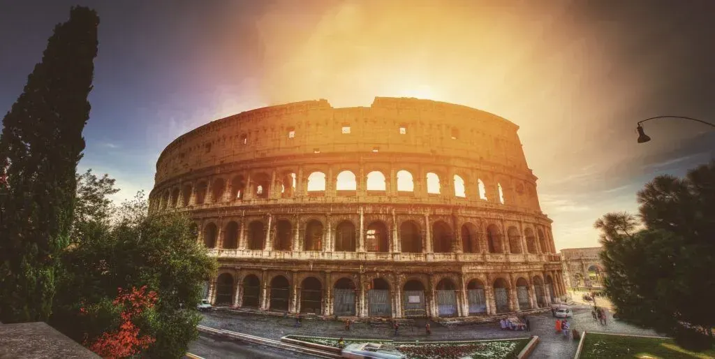 Sunset view of the Colosseum in Rome with warm orange light and surrounding trees