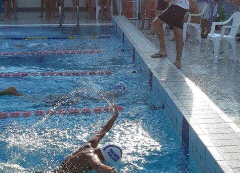 Swimmers racing in a pool, with one person doing a freestyle stroke in the foreground.