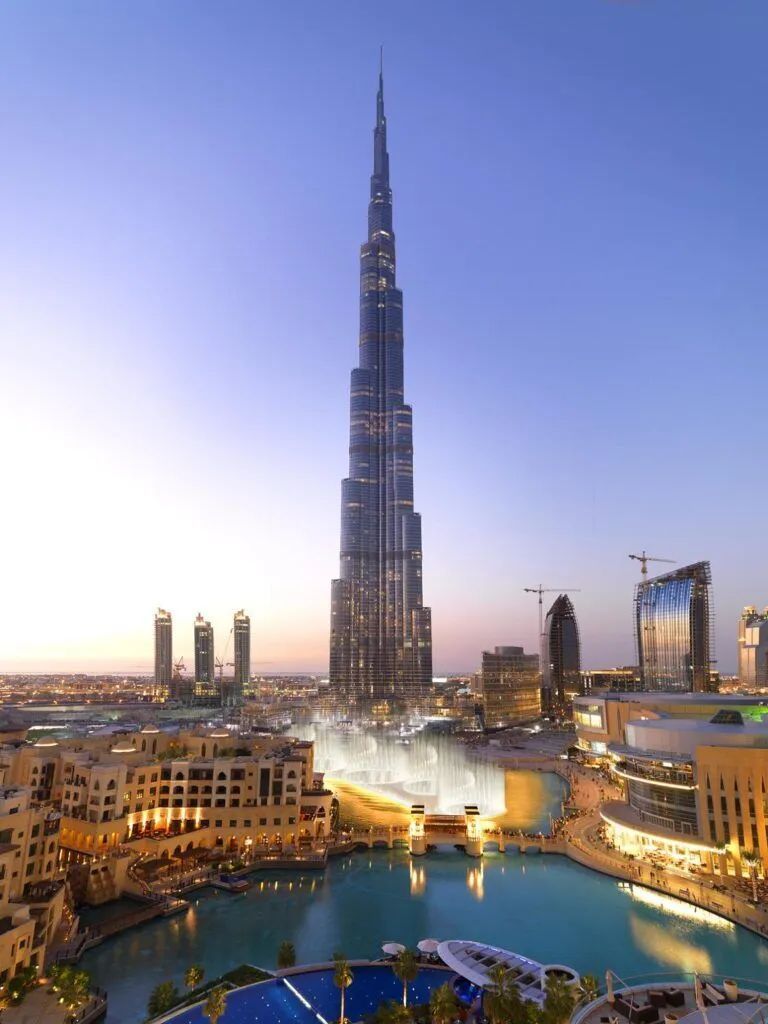Dubai skyline at dusk with Burj Khalifa above illuminated fountains and surrounding buildings
