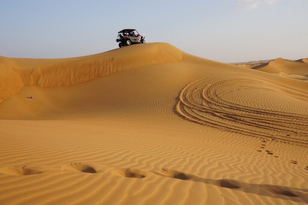 ATV on a golden sand dune under a clear blue sky with tire tracks in the desert
