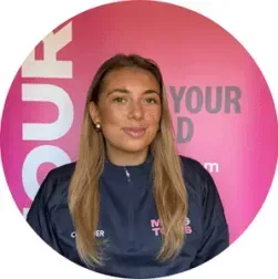 Portrait of a woman in a navy jacket standing before a pink circular branded backdrop