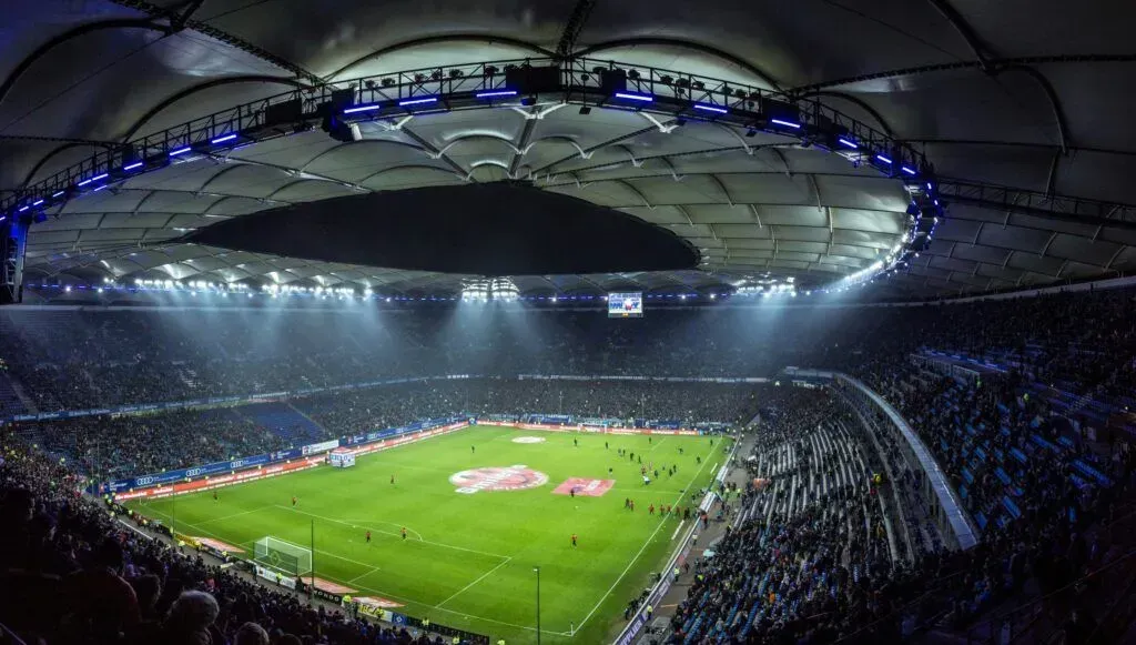 Packed soccer stadium with a green field and bright lights under a domed roof.