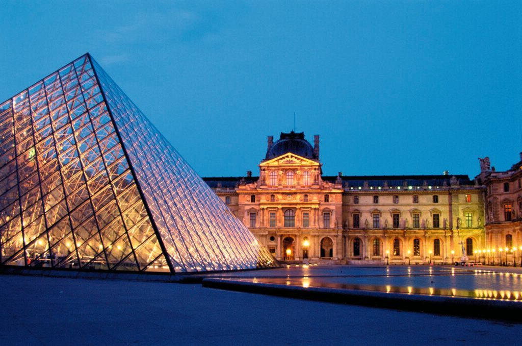 Louvre Pyramid at dusk with the illuminated museum façade reflecting in the water