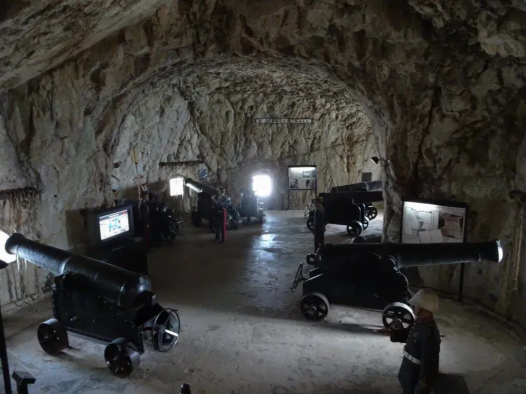 Cannons displayed inside a cave-like museum room with stone walls and bright entrance light