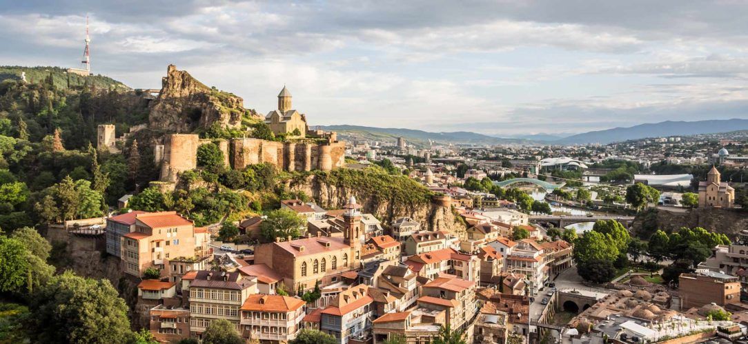 Panoramic view of a historic hilltop city with stone ruins, church domes, and dense terracotta-roofed buildings