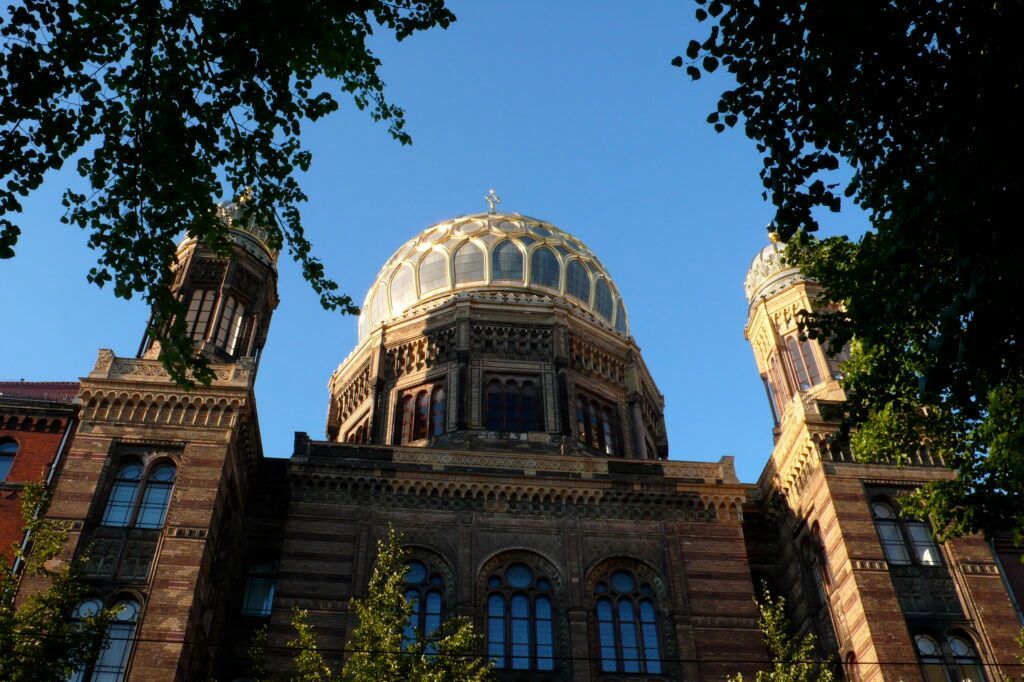 Historic stone building with a domed roof framed by trees against a blue sky