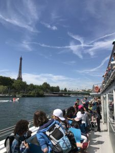Tourists seated on a boat cruise along a river with the Eiffel Tower in the distance under a blue sky