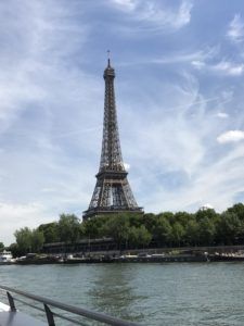 Eiffel Tower rising above trees beside the Seine under a partly cloudy sky