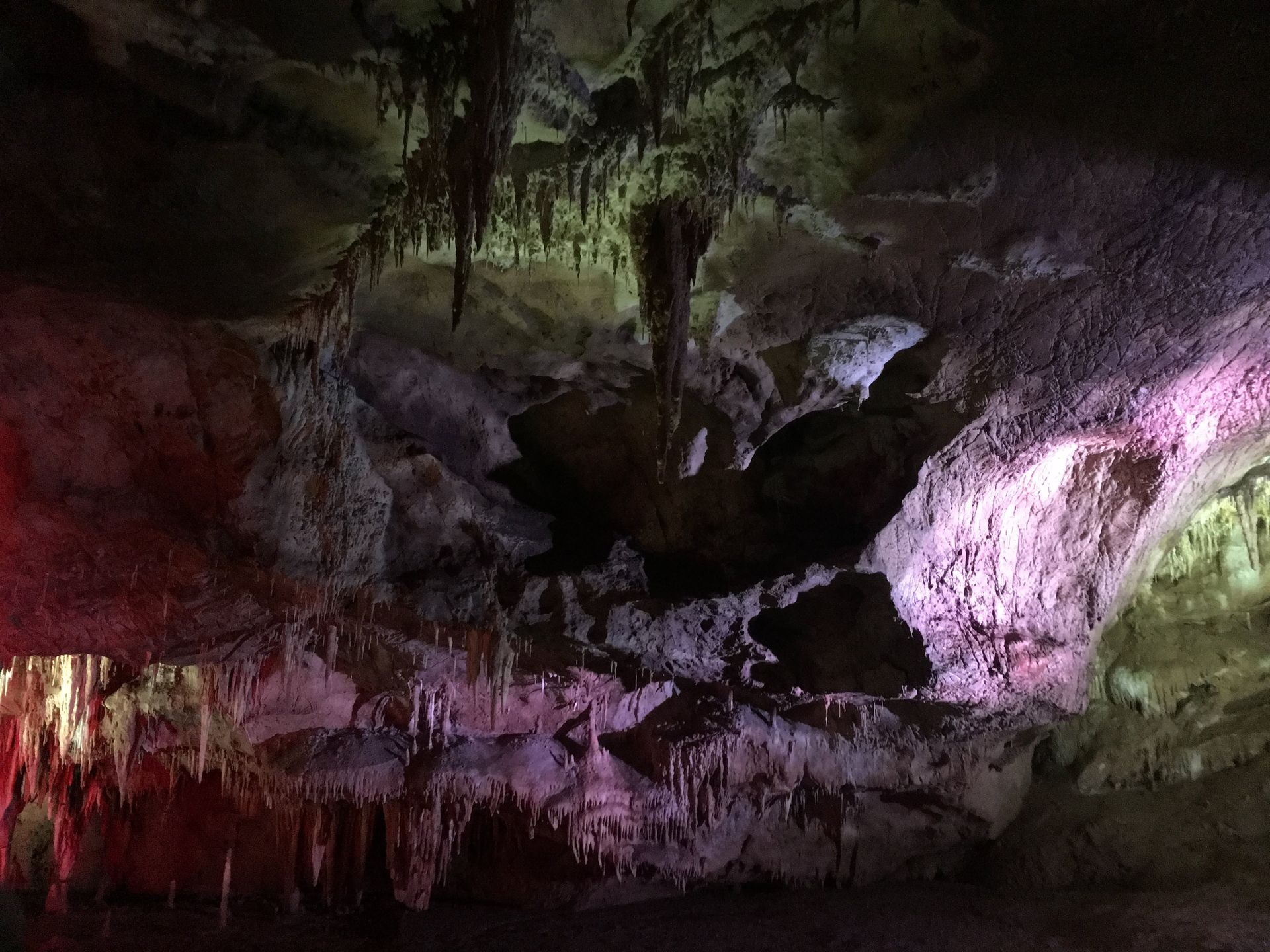 Color-lit cave interior with rugged rock formations and stalactites in red, green, and purple light