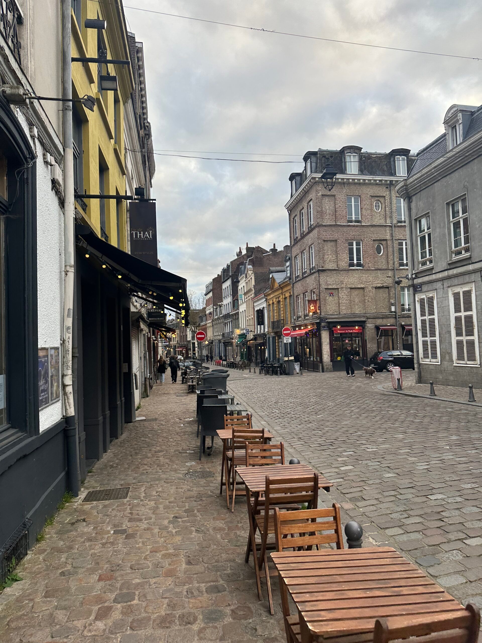 Cobblestone street with outdoor café tables beside historic buildings on a cloudy day